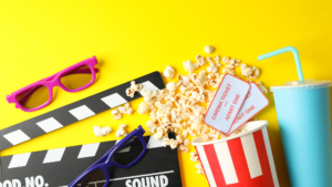 image shows a movie clapper, popcorn, sunglasses, and a drink on a yellow background