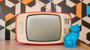 image shows a vintage television and cat ornament on a table with vintage geometric wallpaper in the background