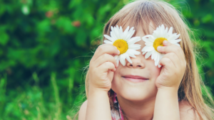 image shows a girl smiling with daisies covering her eyes